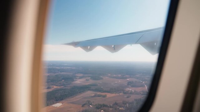 Handheld airplane-window view during rough flight, with visible wing shake, turbulence, and farmland below capturing an uneasy in-air travel moment.