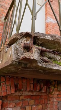 Vertical close-up of a severely damaged concrete balcony edge with rusted steel and cracked brick support, highlighting structural failure, corrosion, and unsafe building neglect.