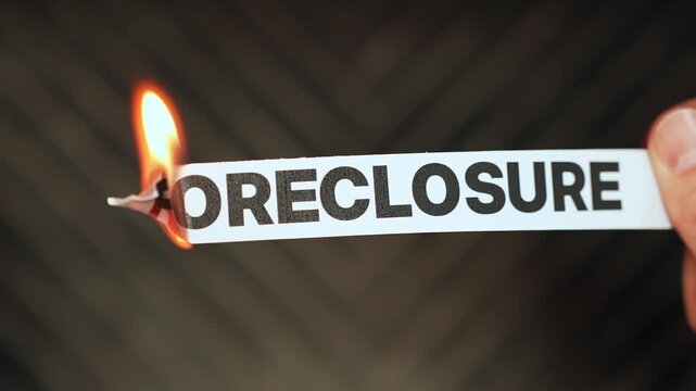 Burning &ldquo;foreclosure&rdquo; label held by hand, symbolizing mortgage relief, saving a home, financial recovery, and protection from housing loss or forced sale.