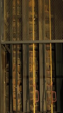 Vertical backstage theater rigging with fly system ropes, counterweight frames, and brick wall details, revealing technical stage infrastructure behind a live performance venue.