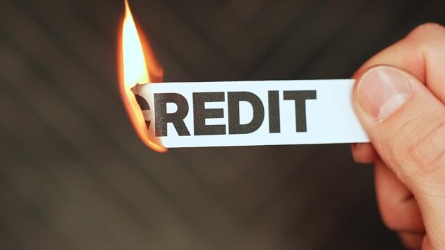 Burning &ldquo;credit&rdquo; label held by hand, symbolizing debt freedom, cash-based living, financial independence, and release from borrowing pressure or credit dependence.