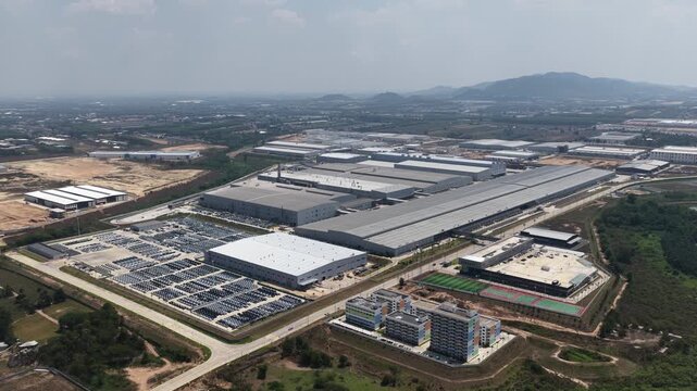 Modern electric automotive manufacturing plant with expansive parking lots filled with newly produced vehicles ready for distribution and export in an industrial zone. Phananikhom, Thailand.