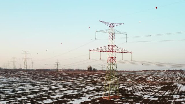 Electricity pylons and cables crossing a snow-covered landscape under warm sunset light.