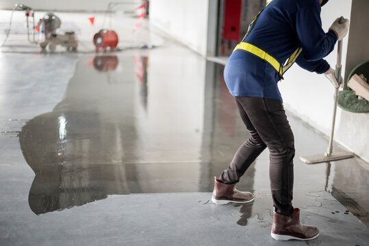 Construction worker painting epoxy flooring or floor hardener