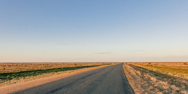 Endless bitumen road stretching into the horizon under a vast, clear blue sky