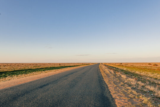 Long, empty bitumen road stretching into the horizon under a clear blue sky