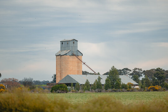 Old agricultural silo and farm buildings stand against a cloudy sky in a rural landscape