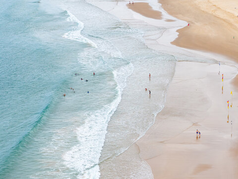 Aerial view of people walking through gentle waves rolling onto a sandy beach