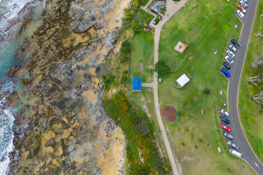 Aerial view of a carpark in a green coastal reserve above a rocky beach