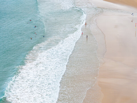 Aerial view of people walking through gentle waves rolling onto a sandy beach