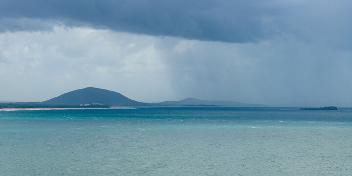 Aerial panorama view of rain falling from dark clouds over a calm turquoise sea and hills