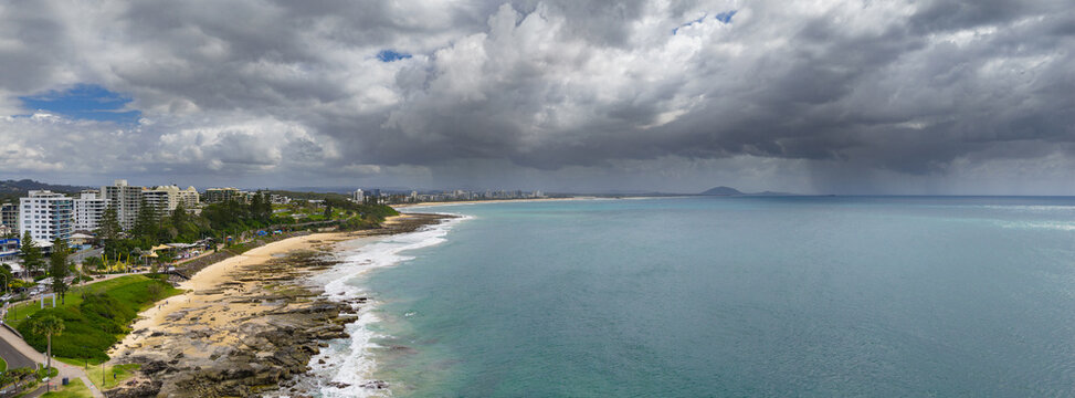 Aerial panorama view of rain falling from dark clouds approaching over a coastal waterfront