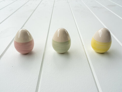 Three ceramic easter eggs with pastel stripes on white timber table top
