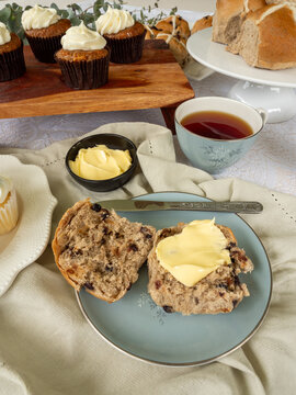 Hot cross buns and carrot cake on wooden platter with cup of tea and linen napkin