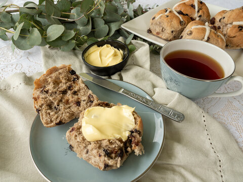 Hot cross buns with butter on linen napkin with cup of tea and eucalyptus branch