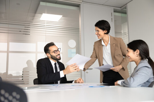 Smiling businesswoman sharing handout sheets, project materials, documents or business report to colleagues during briefing in conference room. Paperwork, negotiations, collaborative office meeting