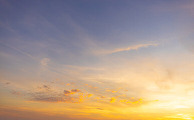 Fototapeta premium Beautiful sunset sky with golden light and purple clouds over the horizon,Dramatic sunset sky background with soft orange sunlight and scattered dark clouds during twilight. The evening atmosphere.