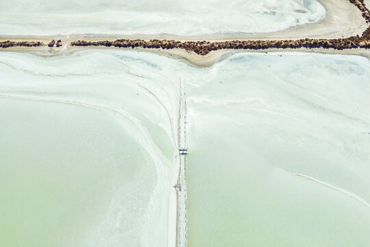 Aerial view of crusty edges around a fenceline running through a pastel green salt lake