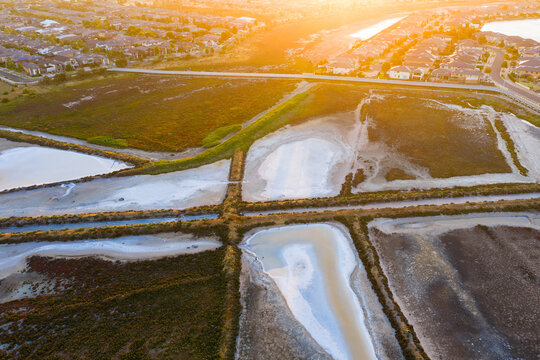 Aerial view of coastal salt ponds and levee banks near the edge of suburban housing