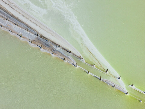 Aerial view of crusty edges around a fenceline running through a pastel green salt lake