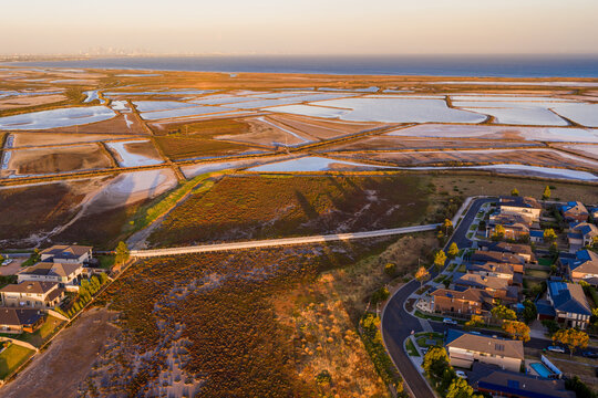 Aerial view of coastal salt ponds and levee banks near the edge of suburban housing