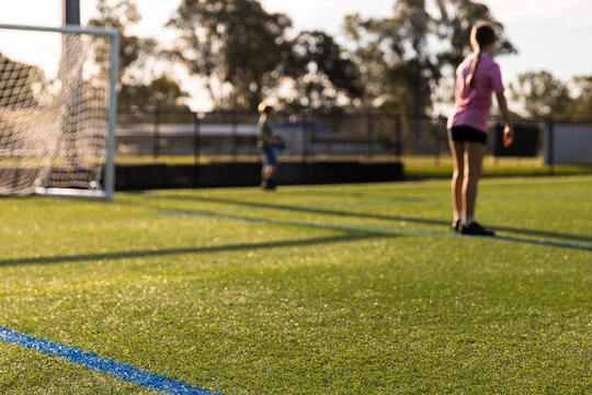 focus on foreground kids playing soccer on artificial turf field