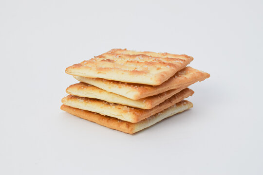 Stack of crispy square crackers isolated on white background, showing golden baked texture, snack food concept, and minimal studio composition.