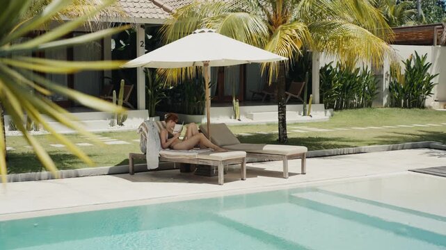 Woman relaxing reading book by poolside at tropical resort