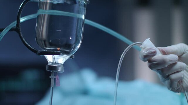 A professional doctor's hand holds a medical syringe to draw liquid from a glass vial for an intravenous IV drip infusion in a sterile white hospital laboratory
