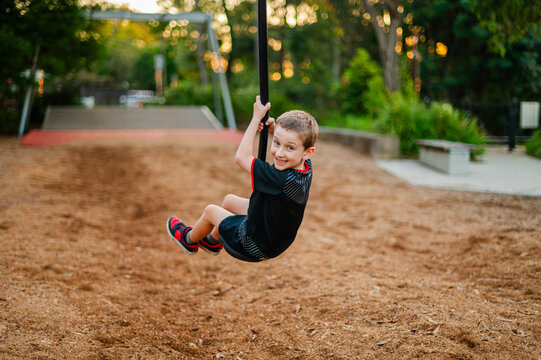 A boy enjoys swinging on a playground zipline as the sun sets