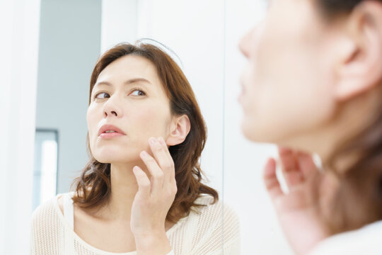 鏡を見てシワを気にするミドルエイジの日本人女性