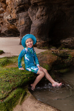 Kid splashing legs in water of rockpool at Caves Beach Newcastle wearing sun safe swimwear