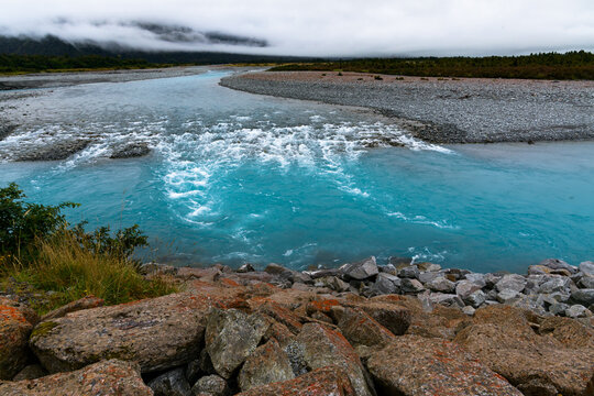 View of rapids and turquoise coloured water with red lichen covered rocks in the foreground