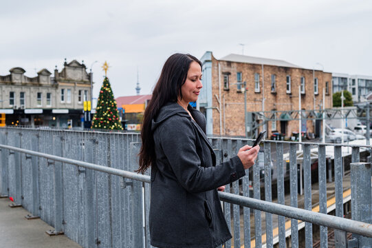 Indonesian woman standing on the pedestrian bridge over city transit area checking her phone