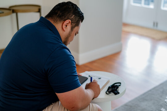 Samoan man writing on a small round table in the living room