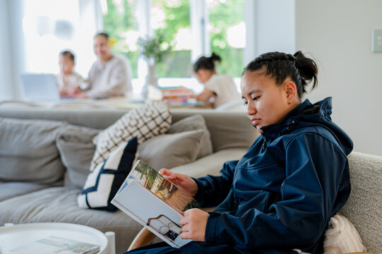 Teenage Samoan girl sitting comfortably on the couch reading a book in the living room