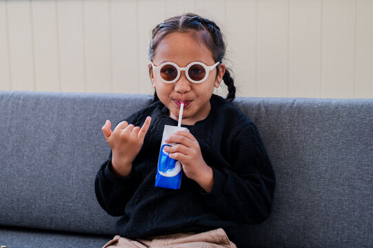 Young Samoan boy wearing round sunglasses sitting on couch sipping from blue box