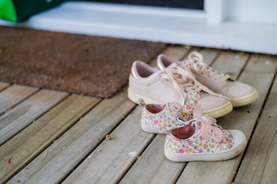 Adult pink sneakers and child floral shoes on wooden deck