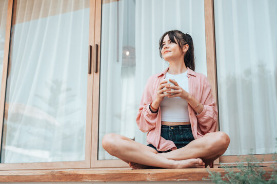 Young woman relaxing on a terrace at home, holding a cup and enjoying a calm moment. Concept of wellness, good health, wellbeing, and balanced lifestyle in a peaceful environment