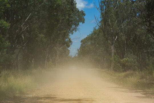 Car kicking up dust while traveling down remote gravel road through bushland