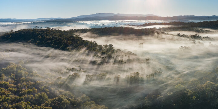 Aerial panorama view of rays of light through fog over a forested valley and distant hills