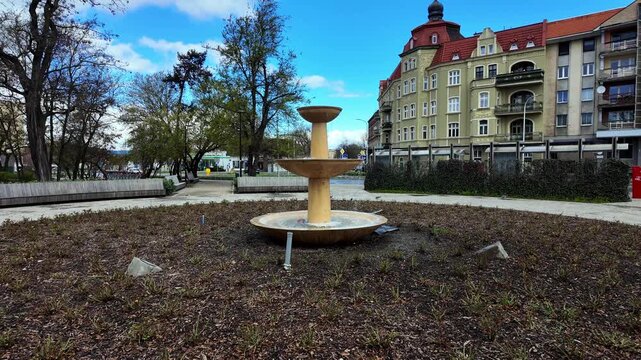 City park fountain with tiered basin in front of a historic tenement building and urban architecture. Sunny spring day, public square, cityscape, urban lifestyle, recreation area, city scenery, landma