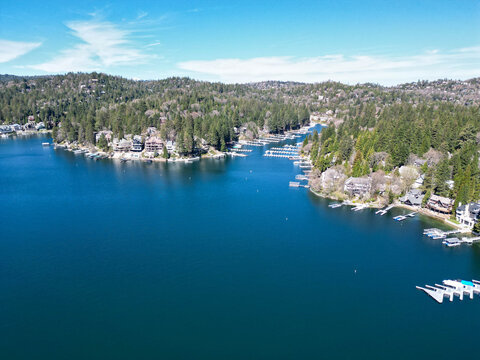 Drone view of a mountain lake surrounded by pine forest and waterfront houses with docks and marina. Suitable for travel, real estate, and outdoor lifestyle themes.
