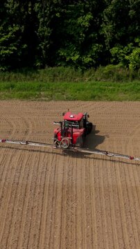 Drone aerial of a tractor applying biological crop treatment with microorganisms and growth stimulators.