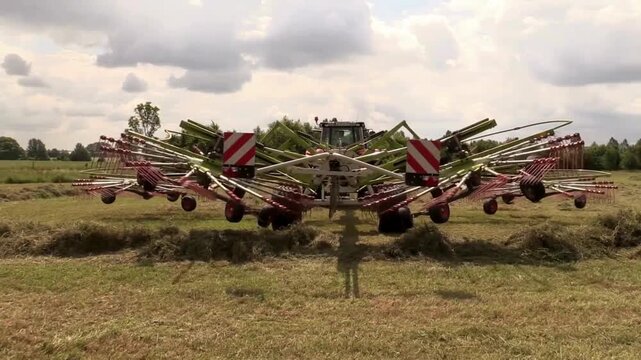 Modern tractor with large rotary rake harvesting hay in field