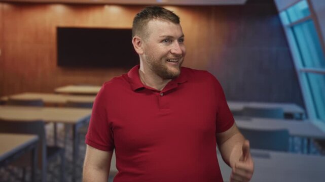 Man in red polo shirt looking sideways with open mouth and thumbs up gesture in a classroom building with desks and window view; surprise humor.