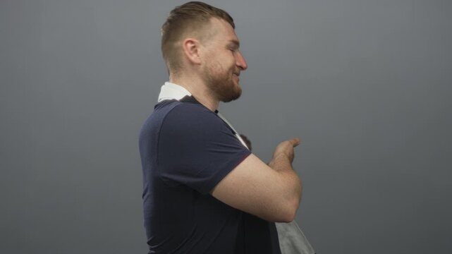 Man with soccer scarf pointing with bare forearm and smiling while turning in gray studio set; cheerful mischief.