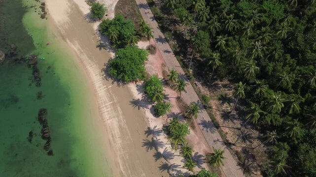 Top down aerial view of scooter riding along tropical coastal road on Koh Jum Thailand with palm trees sandy beach and clear shallow water dynamic island lifestyle travel and freedom concept