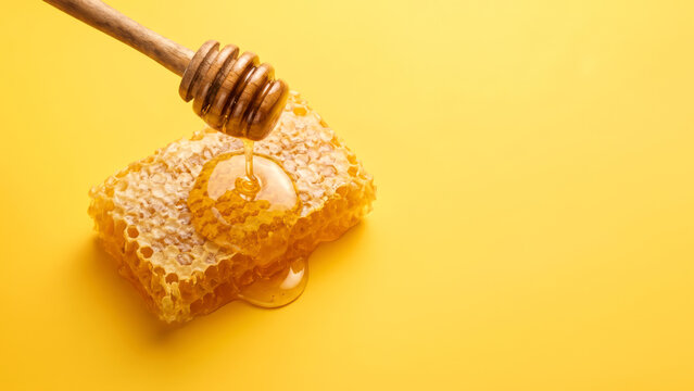 Honeycomb dripping honey from wooden dipper on yellow background, golden and sweet treat