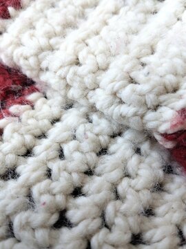 A closeup shot of striped red and white crochet blanket with a bit of wear fuzz. 